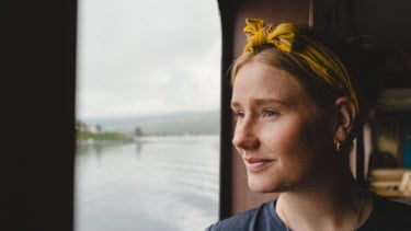 Young woman with scarf on her head looking out of a window